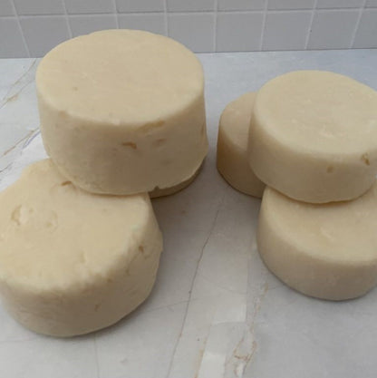 three large and 3 small handmade round shaped shampoo soap bars stacked on a tiled surface