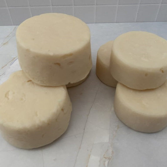 three large and 3 small handmade round shaped shampoo soap bars stacked on a tiled surface