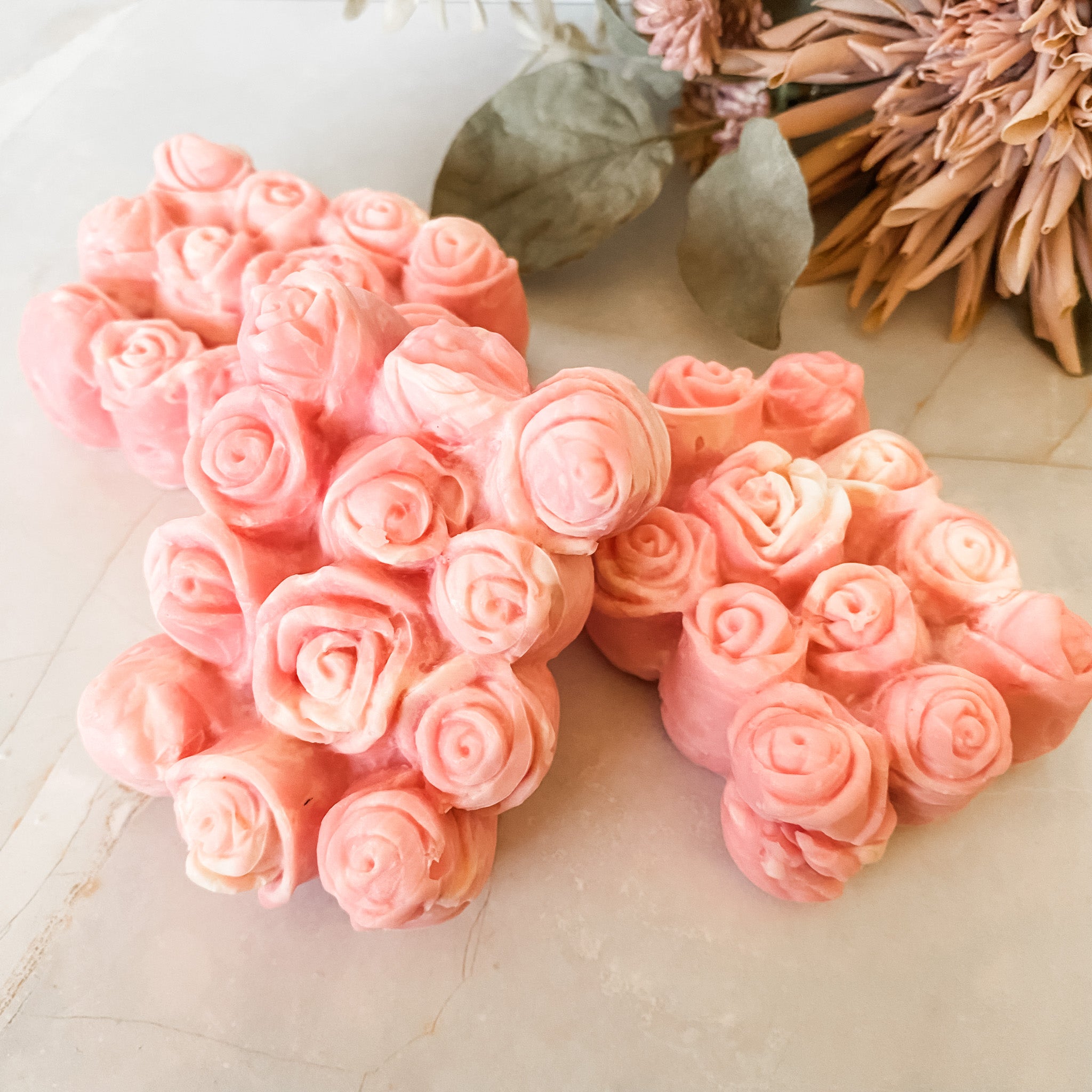 Pink rose-shaped soaps on a light surface with dried flowers in the background.