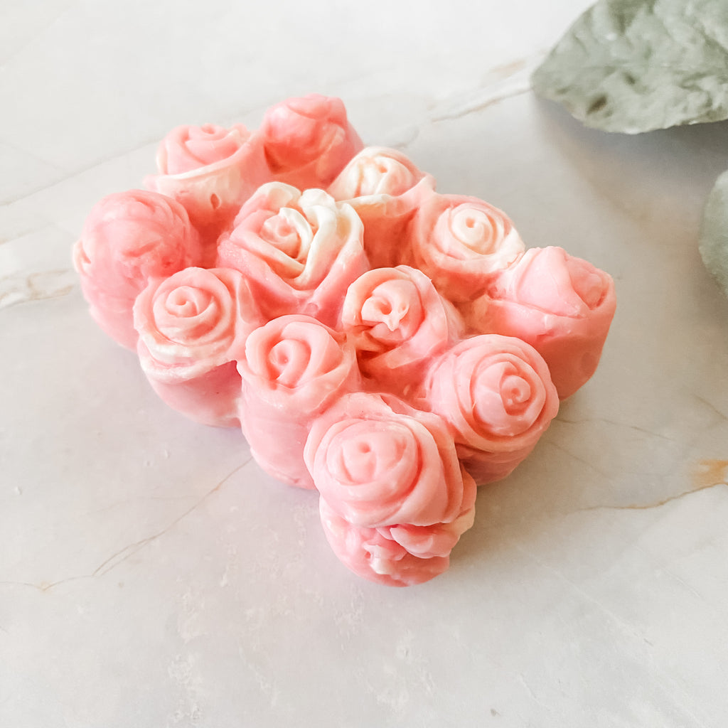 Pink soap bar with 12 rosebuds on a light surface with green leaves.