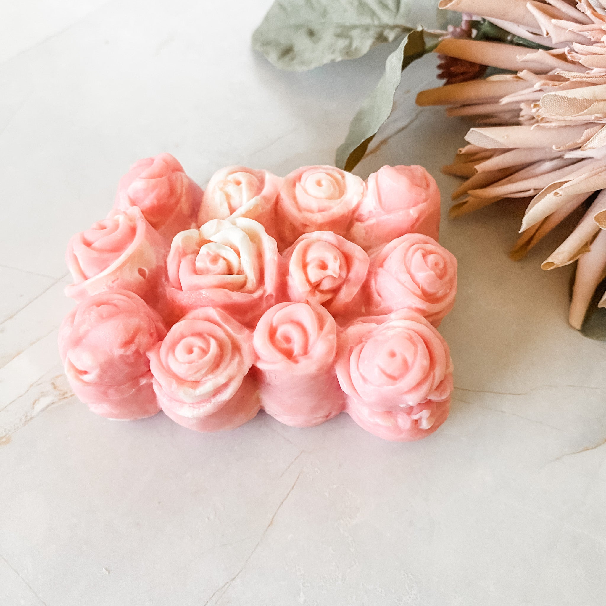 Pink soap bars with 12 rosebuds on a light surface with decor items.