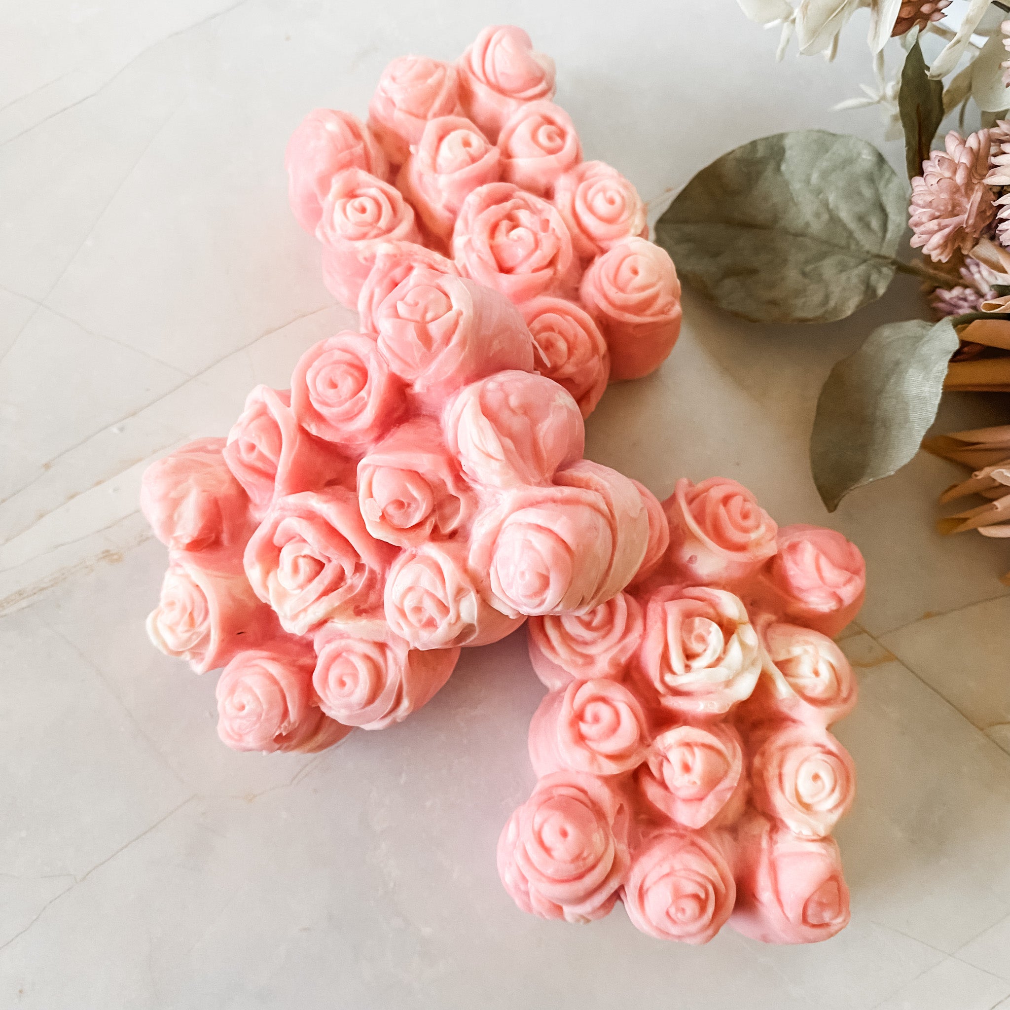 Pink soap bars with 12 rosebuds on a marble surface with green leaves.