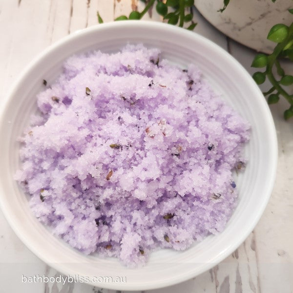 white bowl of pale purple sugar scrub on a light wooden background