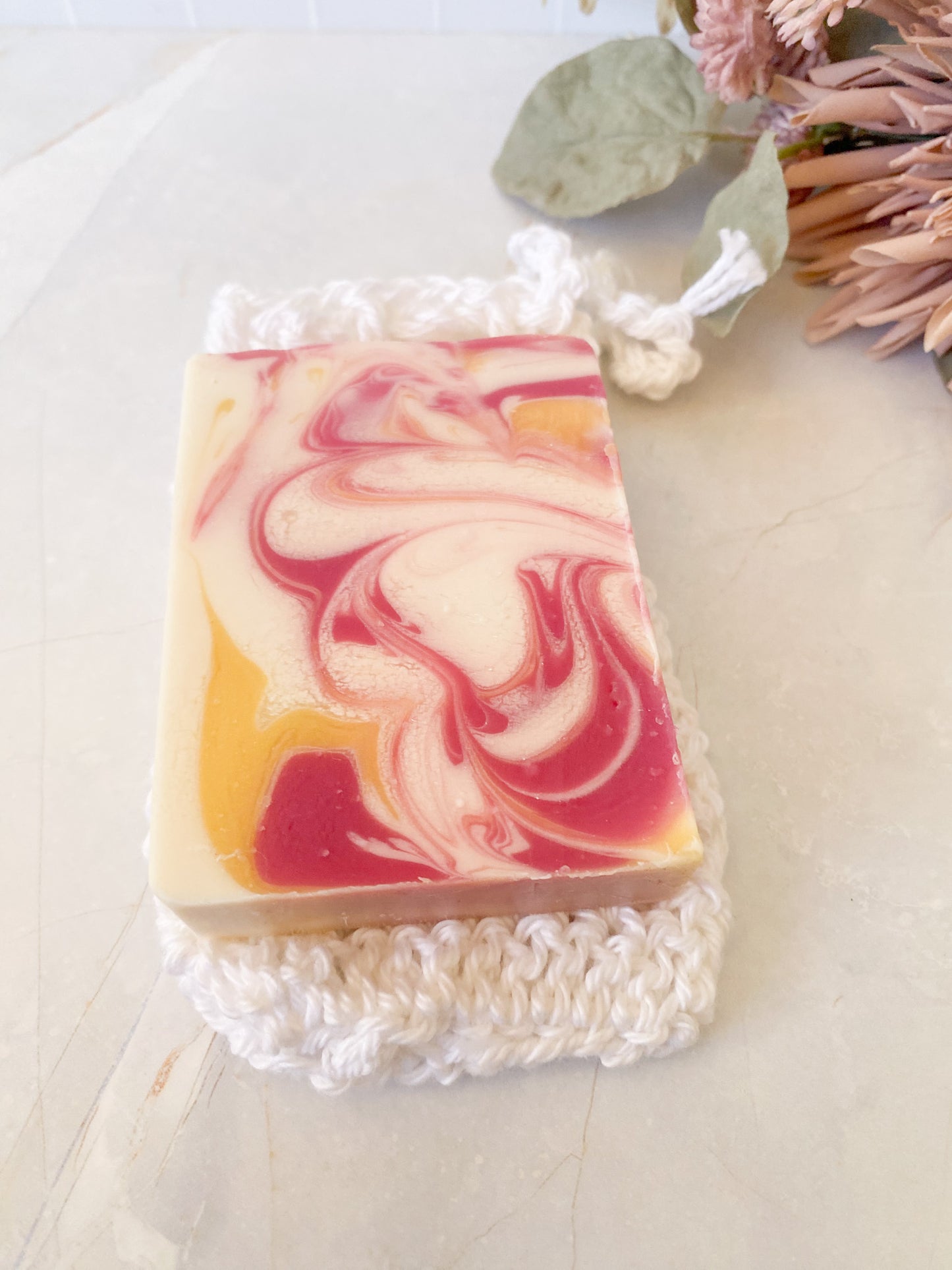 Swirled soap bar with pink and yellow colors on a white crochet soap sack