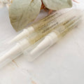 three applicator pens of natural cuticle oil on a marble surface with leaves in the background