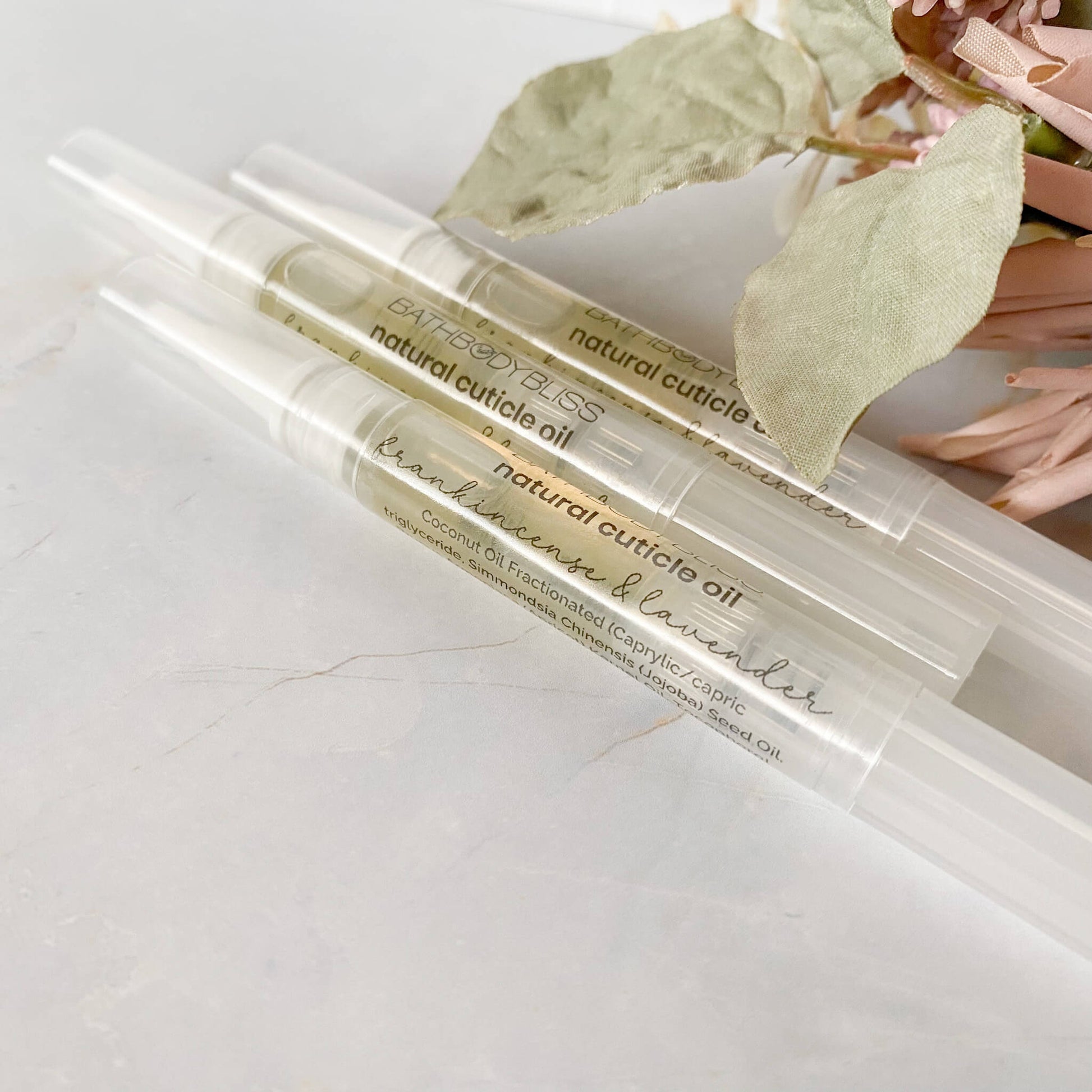 three tubes of natural cuticle oil on a light surface with leaves in the background