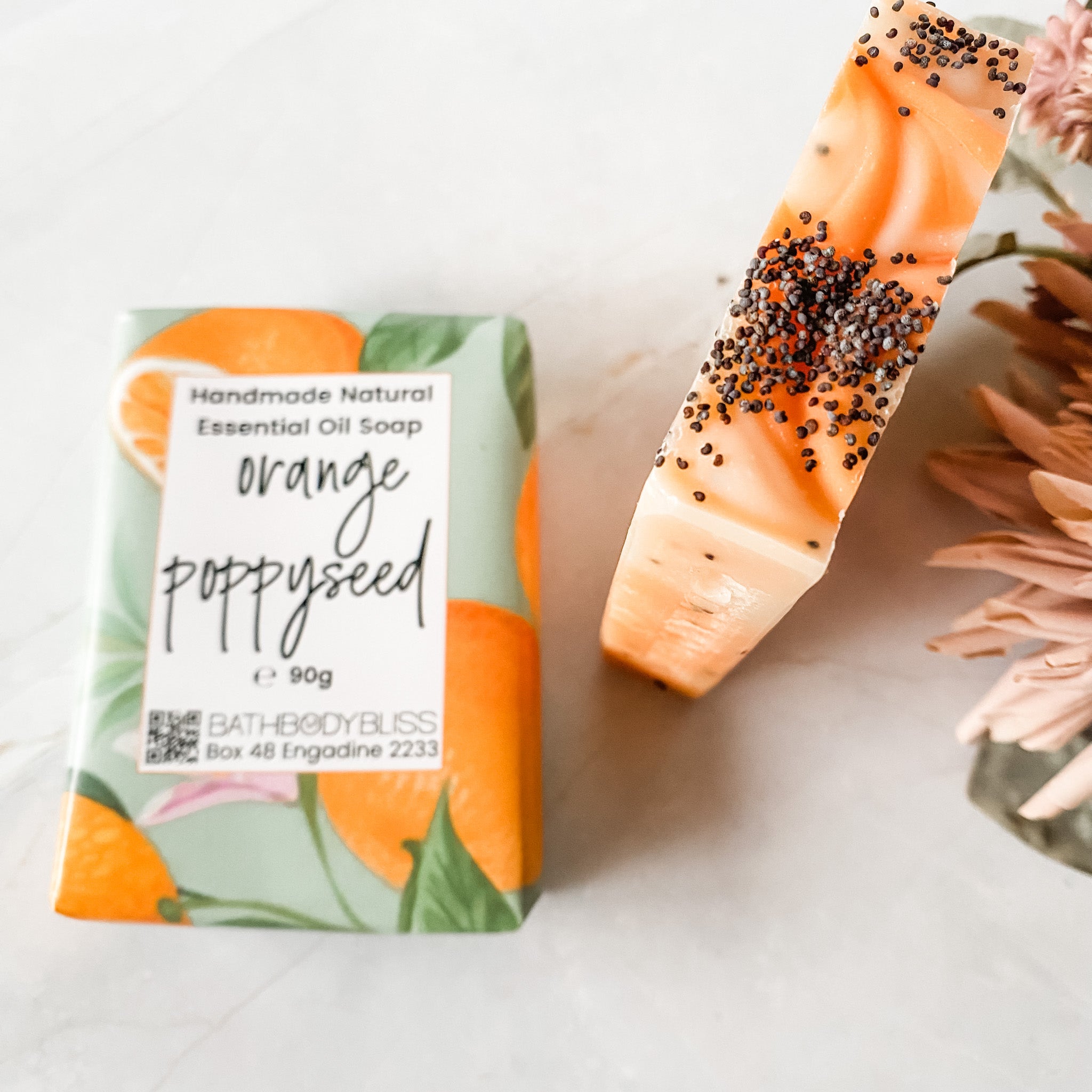 orange poppyseed soap bar in bath body bliss packaging and a standing unwrapped soap bar with orange swirls and poppyseeds on top next to it