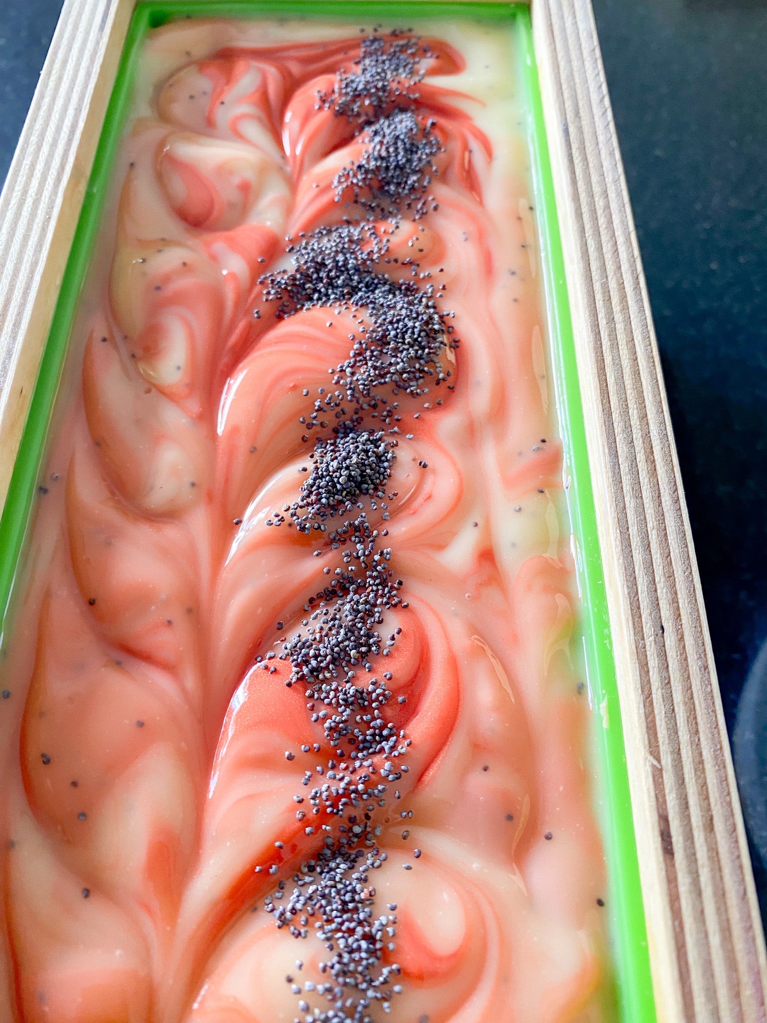 cream and orange swirled soap with poppyseeds in a wooden mould with green silicone liner