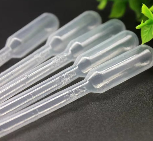 Clear plastic pipettes on a dark surface with green leaves in the background