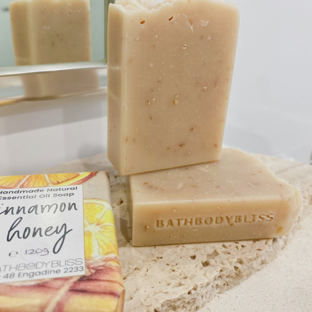 animated image of three handmade cinnamon soap bars, one bar wrapped and two unwrapped, arranged on a stone surface with mirror image in the background