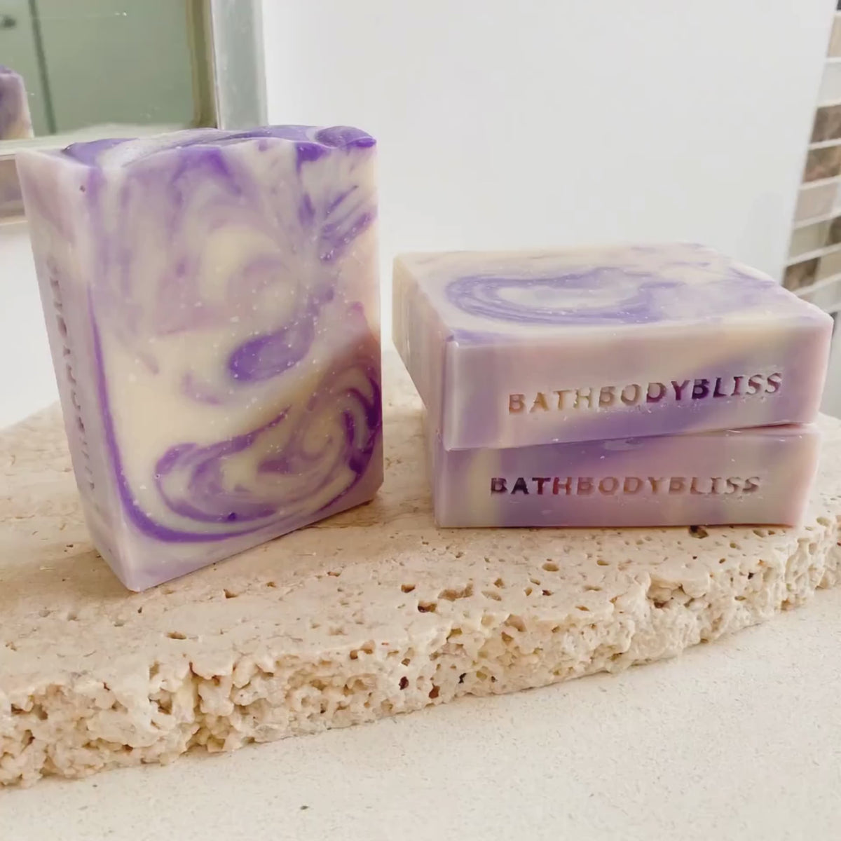 video of three goatsmilk handmade soaps with purple swirls, arranged on a rustic stone