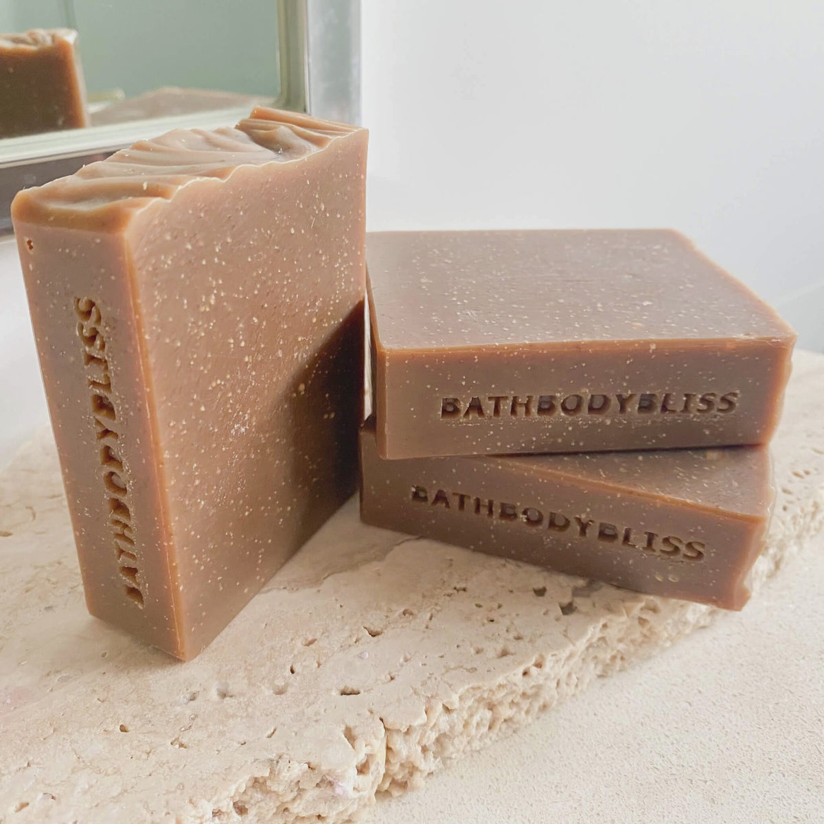 animated photo of 3 unwrapped bars of handmade soap, stamped with bathbodybliss one one side and arranged on a stone surface