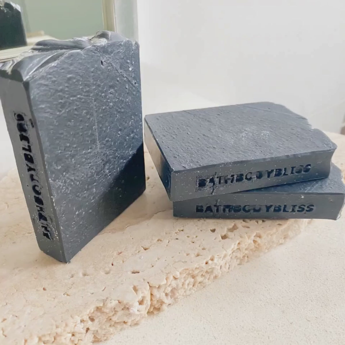 animated image showing three bars of dark grey soap on a stone surface