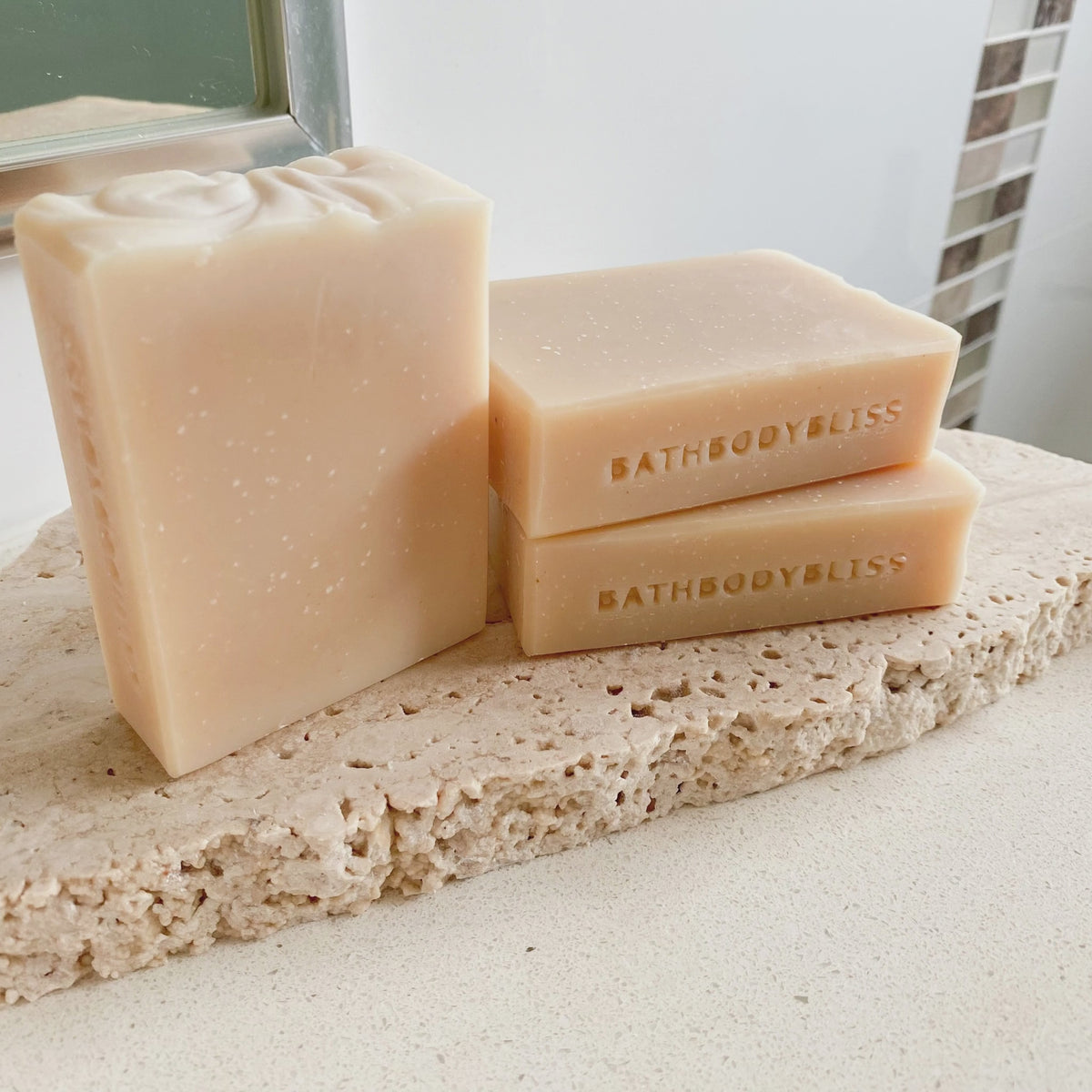 animated photo of three handmade unscented and uncoloured soap bars stamped on the sides with bathbodybliss branding, and arranged on a stone surface
