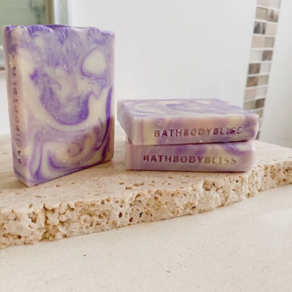 video of three handmade slimcut soaps with purple swirls, arranged on a rustic stone 