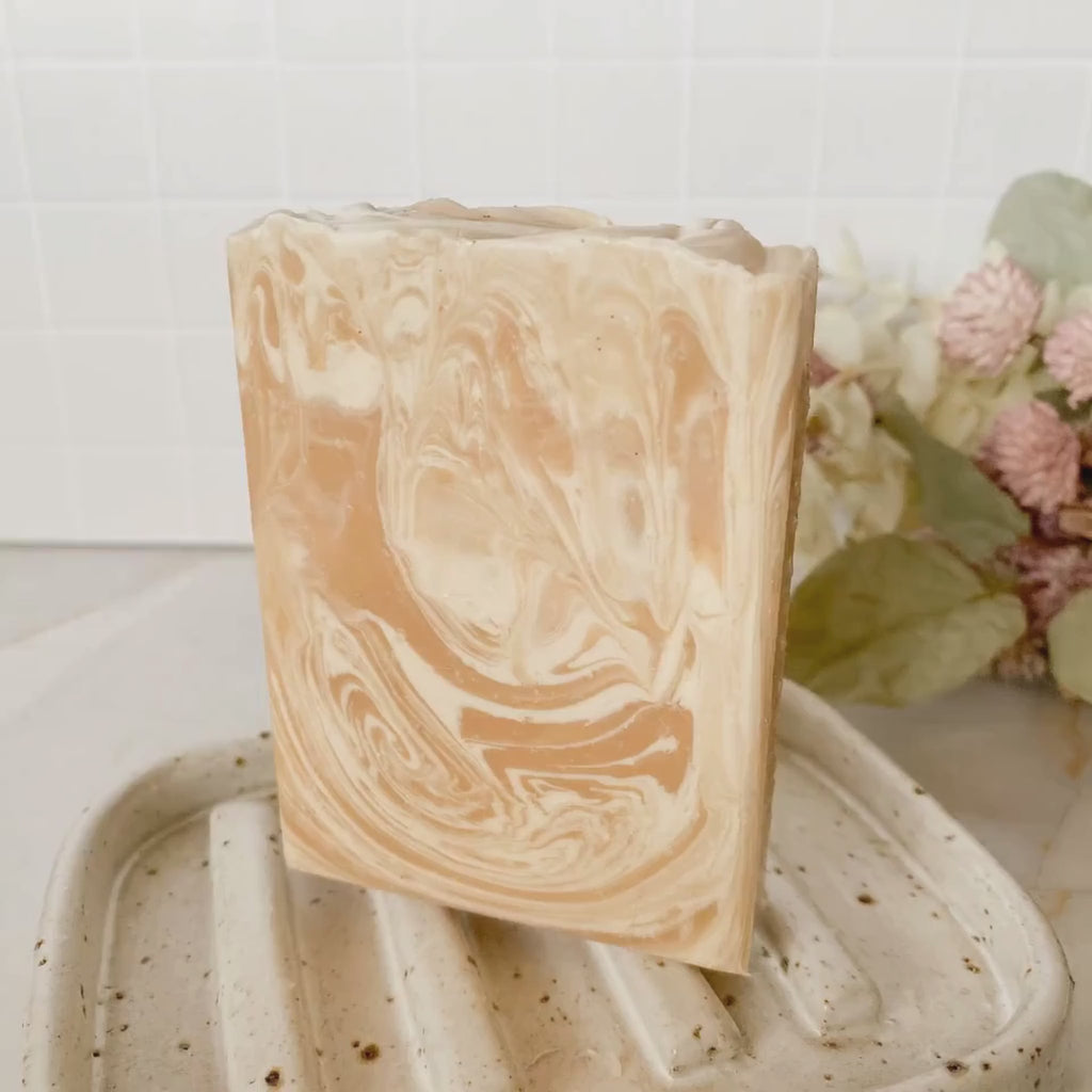 animated image of caramel and white swirled soap on a speckled soap dish with floral decor in the background