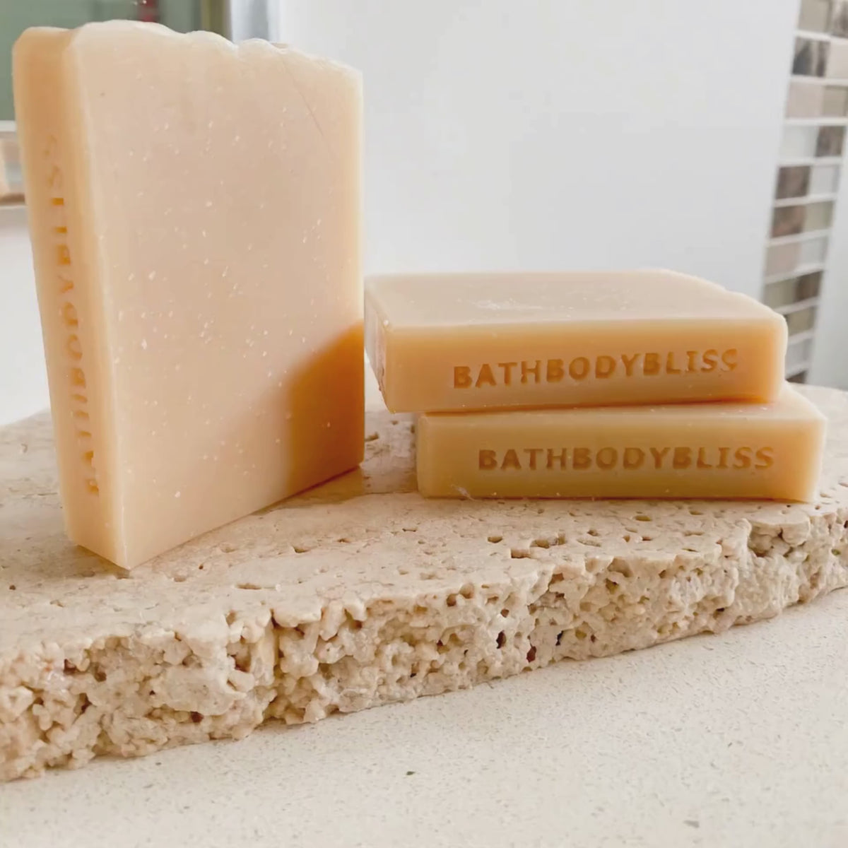 animated photo of three slimcut bars of handmade soap stamped on the sides with bathbodybliss branding, arranged on a rustic stone tile