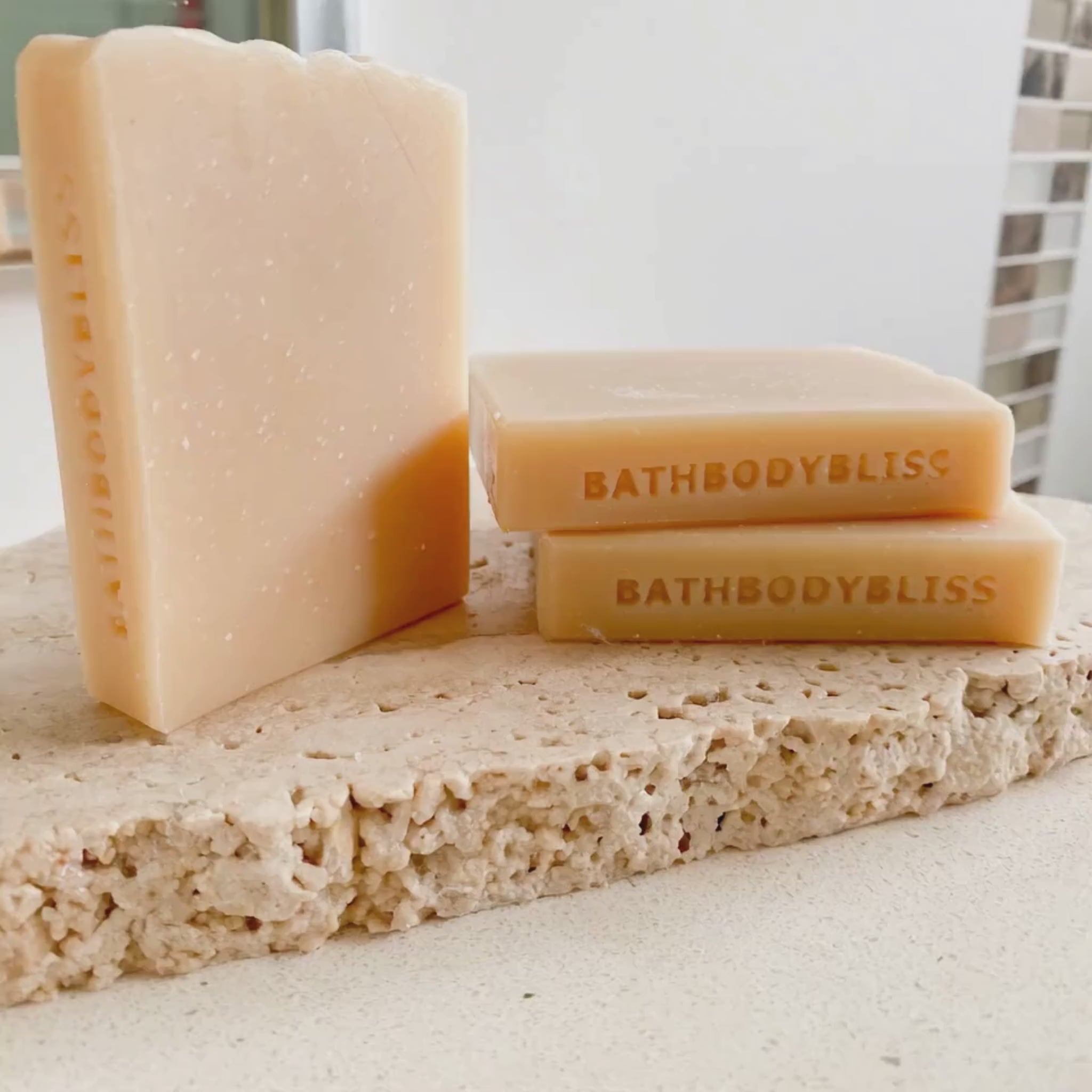 animated photo of three slimcut bars of handmade soap stamped on the sides with bathbodybliss branding, arranged on a rustic stone tile
