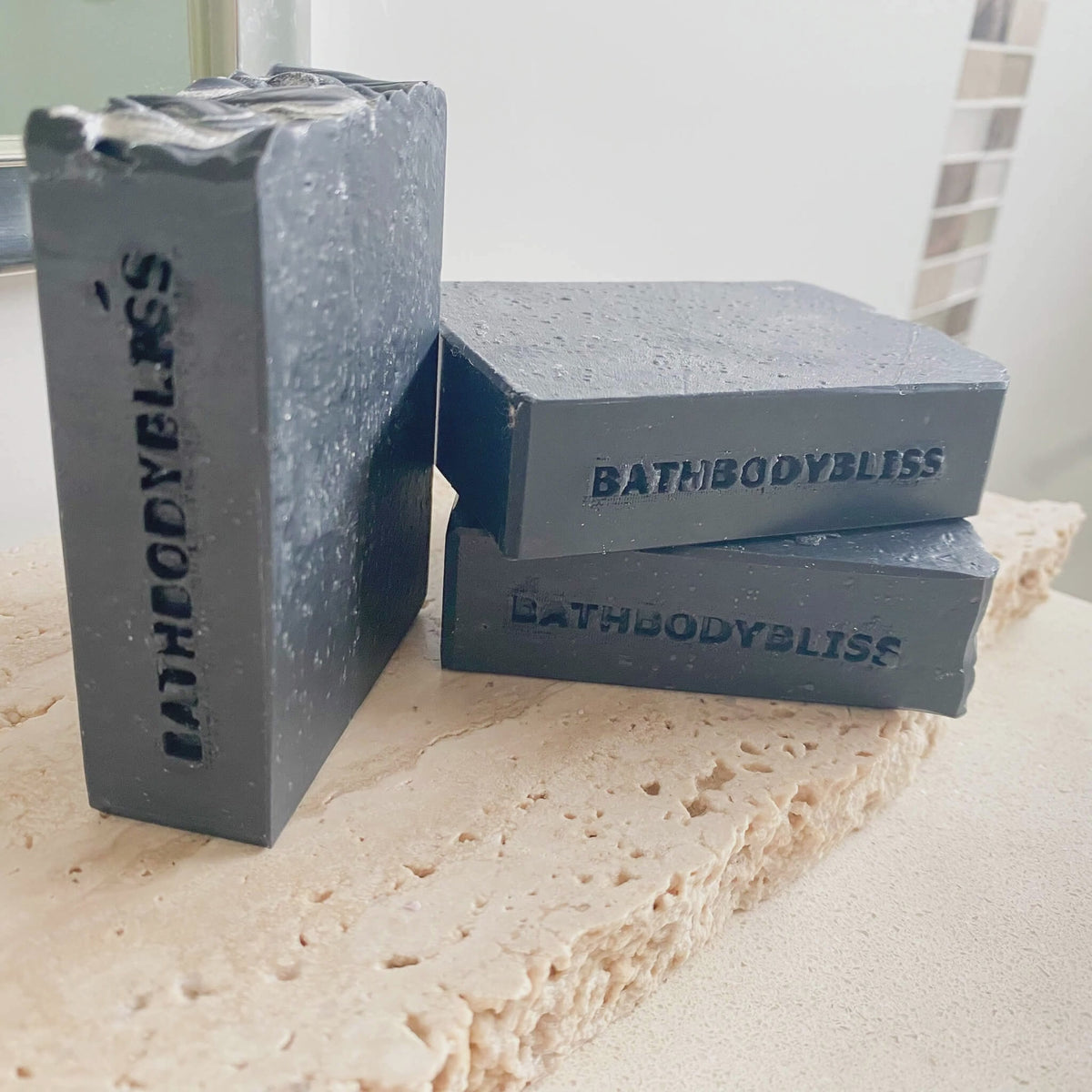 animated image of hree dark grey handmade soap bars with 'bathbodybliss' stamped on each bar