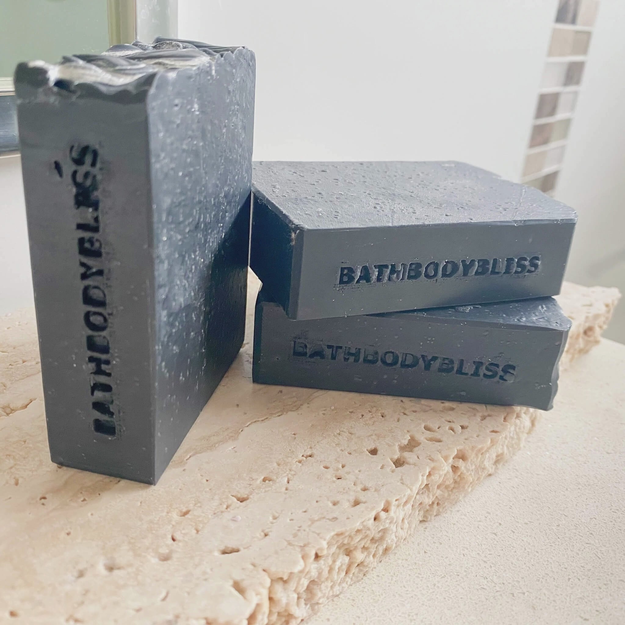 animated image of hree dark grey handmade soap bars with 'bathbodybliss' stamped on each bar