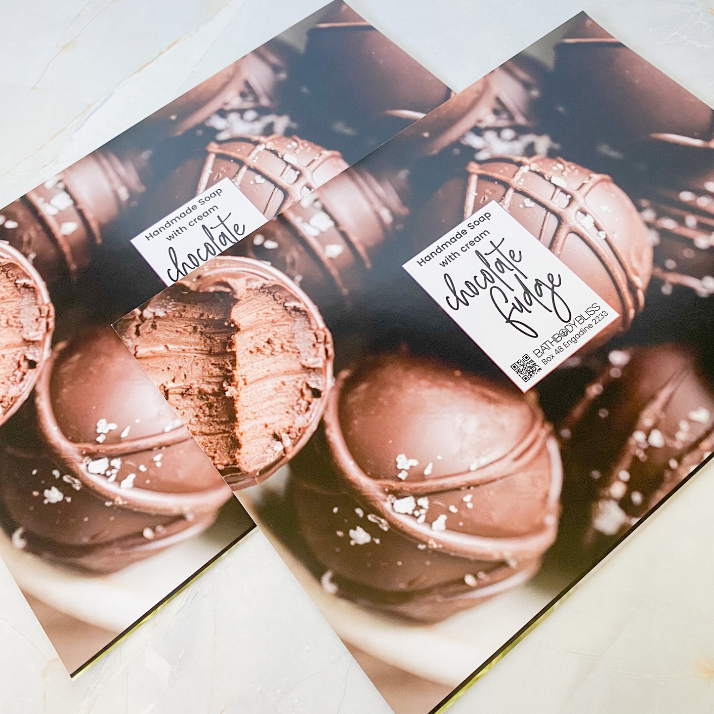 two chocolate fudge soap wrapping papers with bath body bliss branding on a light marble background