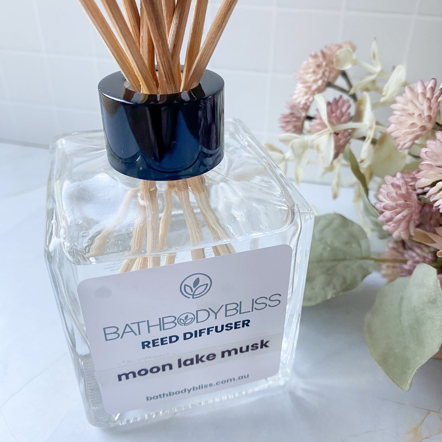 BathBodyBliss reed diffuser with wooden sticks & flowers on a light background