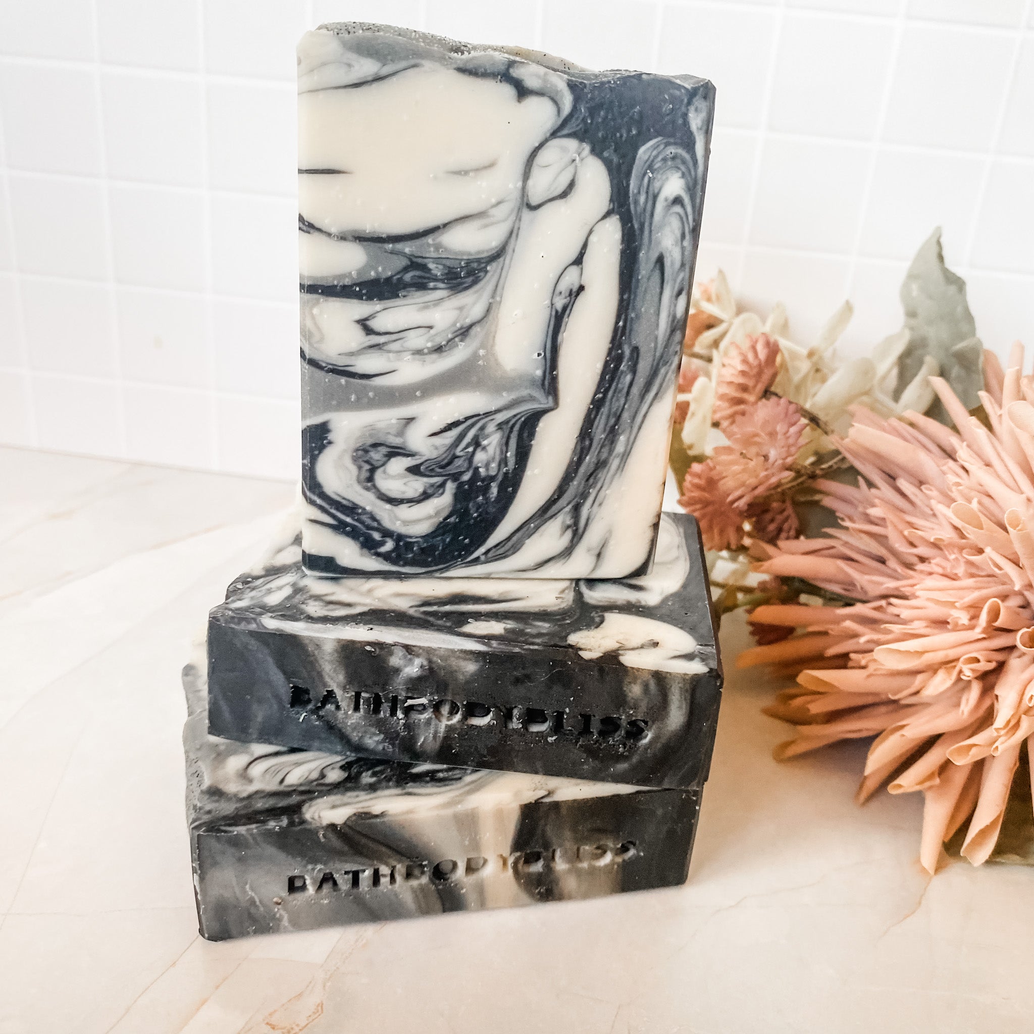 A handmade bar of vegan soap with a swirled gray and white pattern, placed on a surface with a partial view of a floral design to the side.