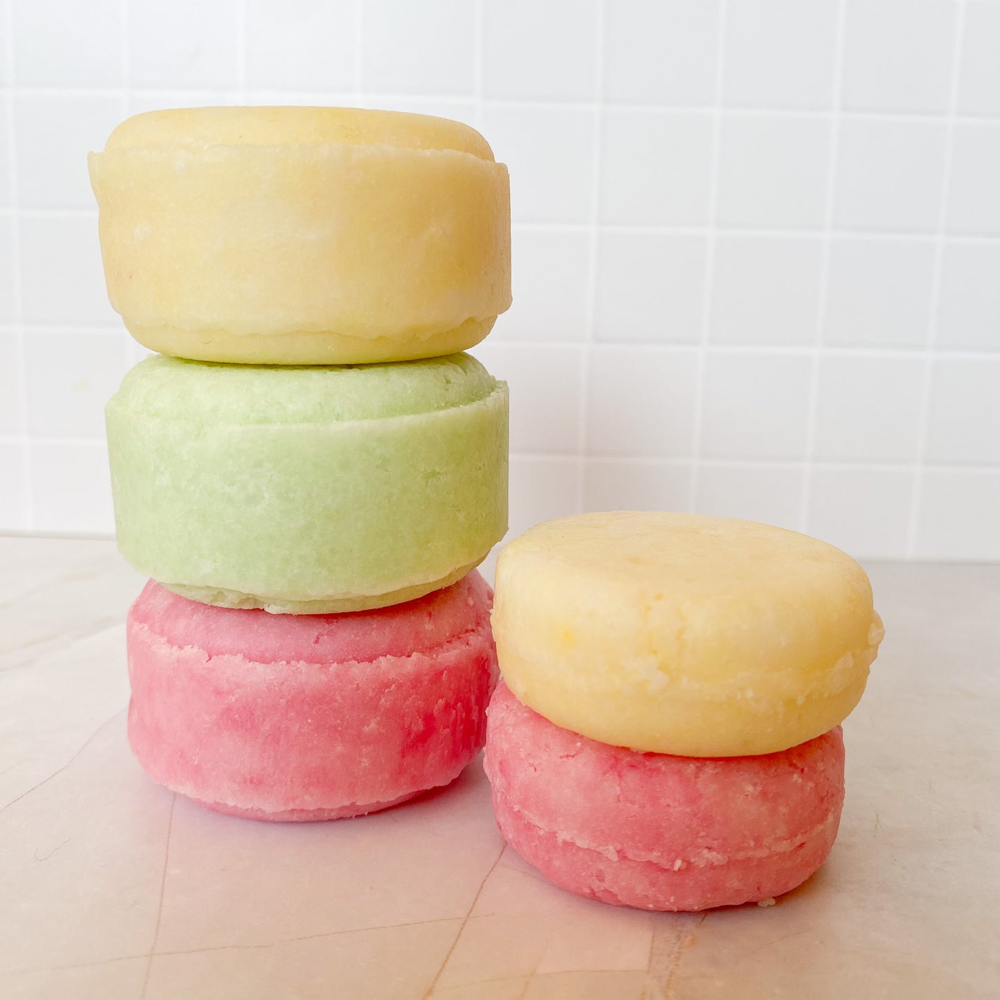 Stack of large and small shampoo bars on a marble surface with white tiles in the background