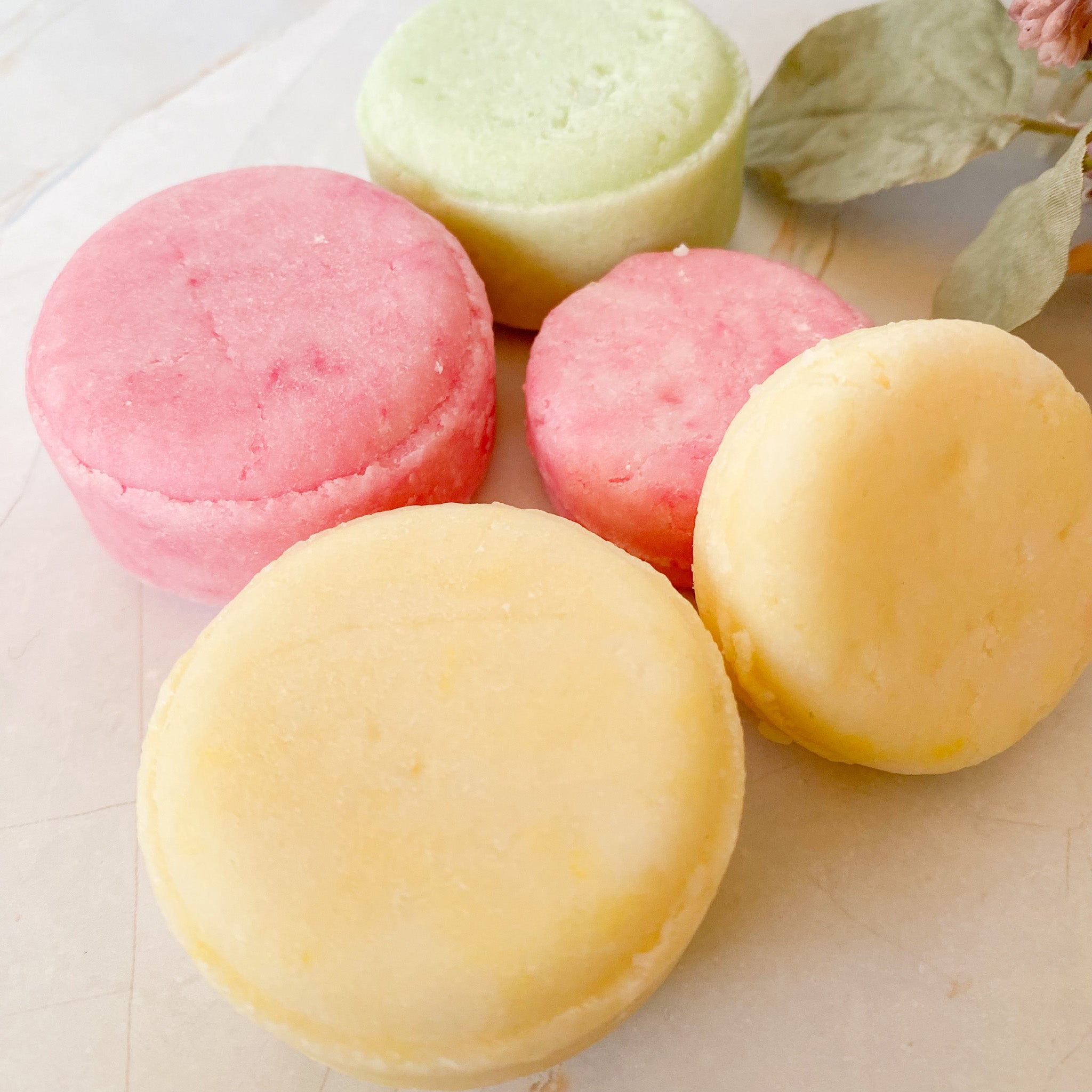 Pastel-colored shampoo bars on a light surface with green leaves.