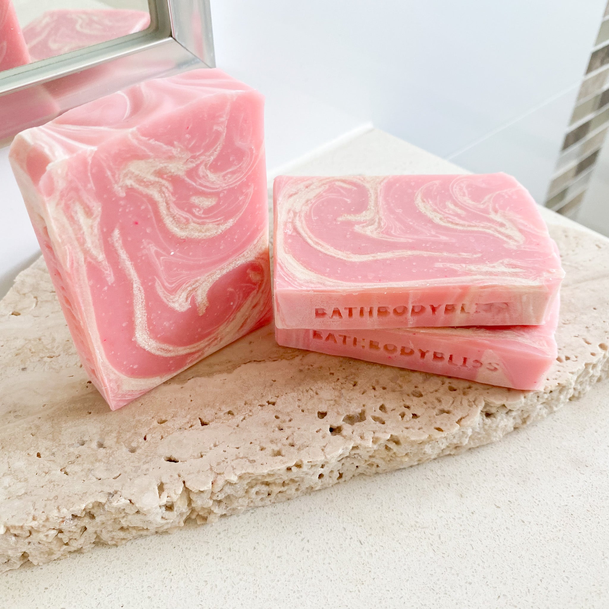 three pink and white swirled soap bars on a pale stone surface