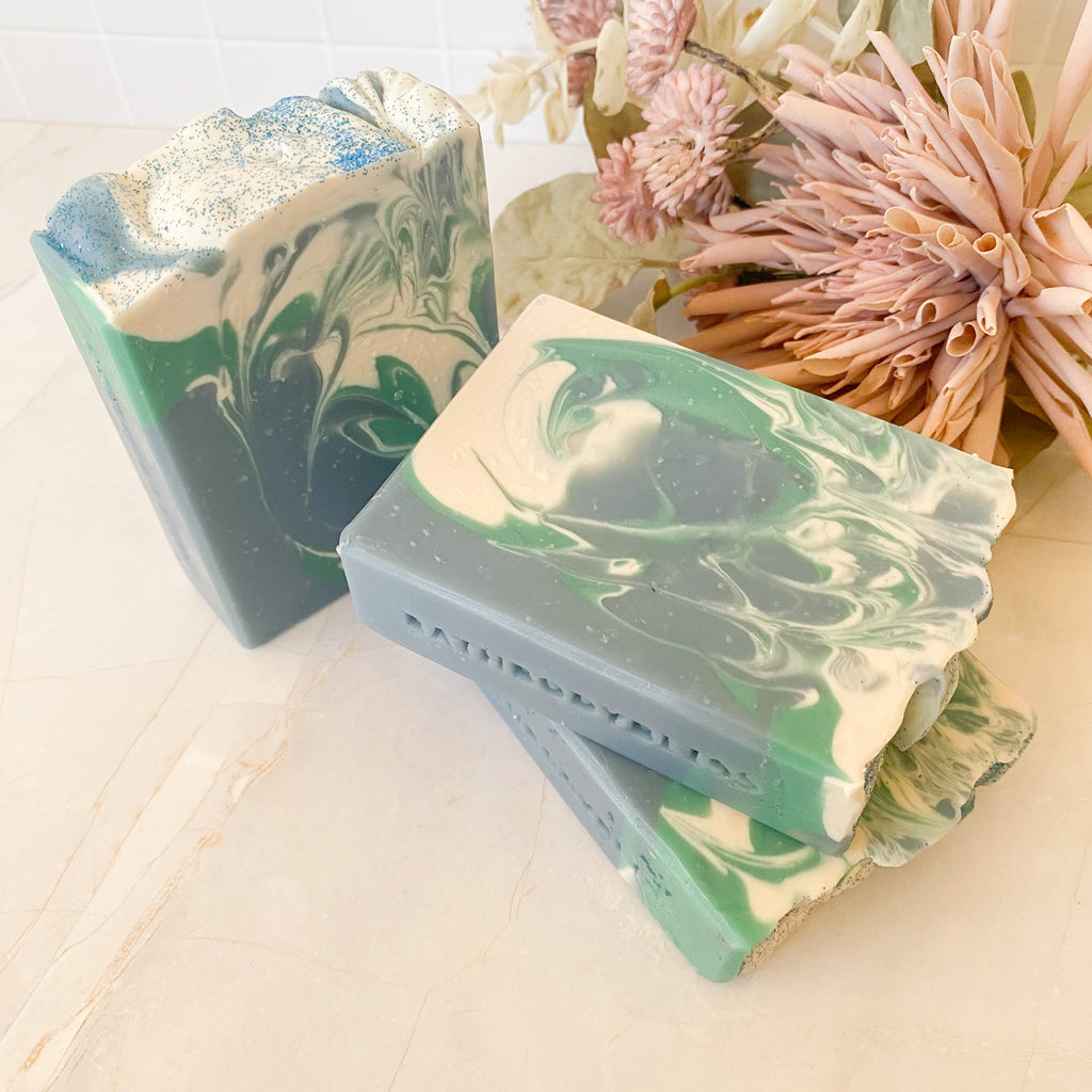 three bars of soap with blue, white and green swirls on a light surface with dried flowers in the background.