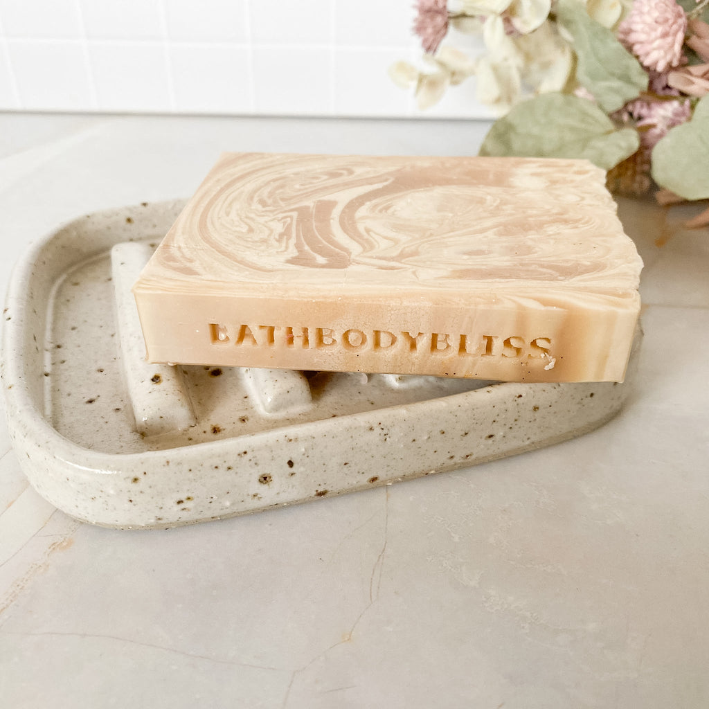 Marble-patterned soap bar with 'BATHBODYBLISS' branding on a speckled ceramic soap dish.