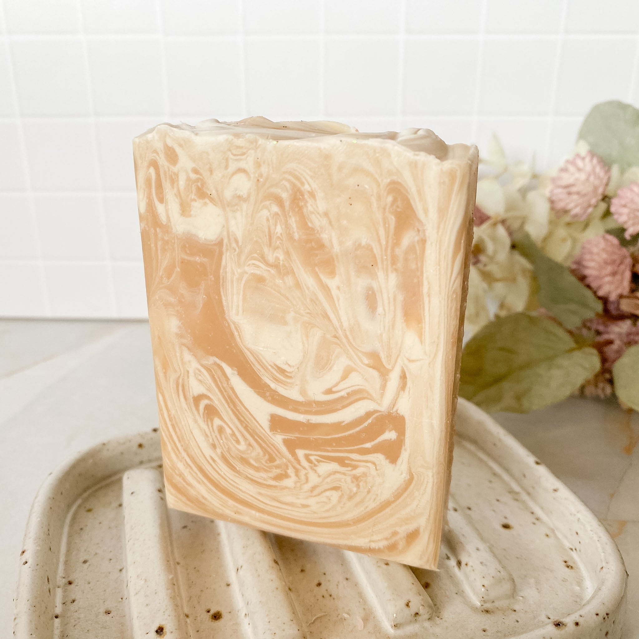 Marbled soap bar on a textured surface with flowers in the background