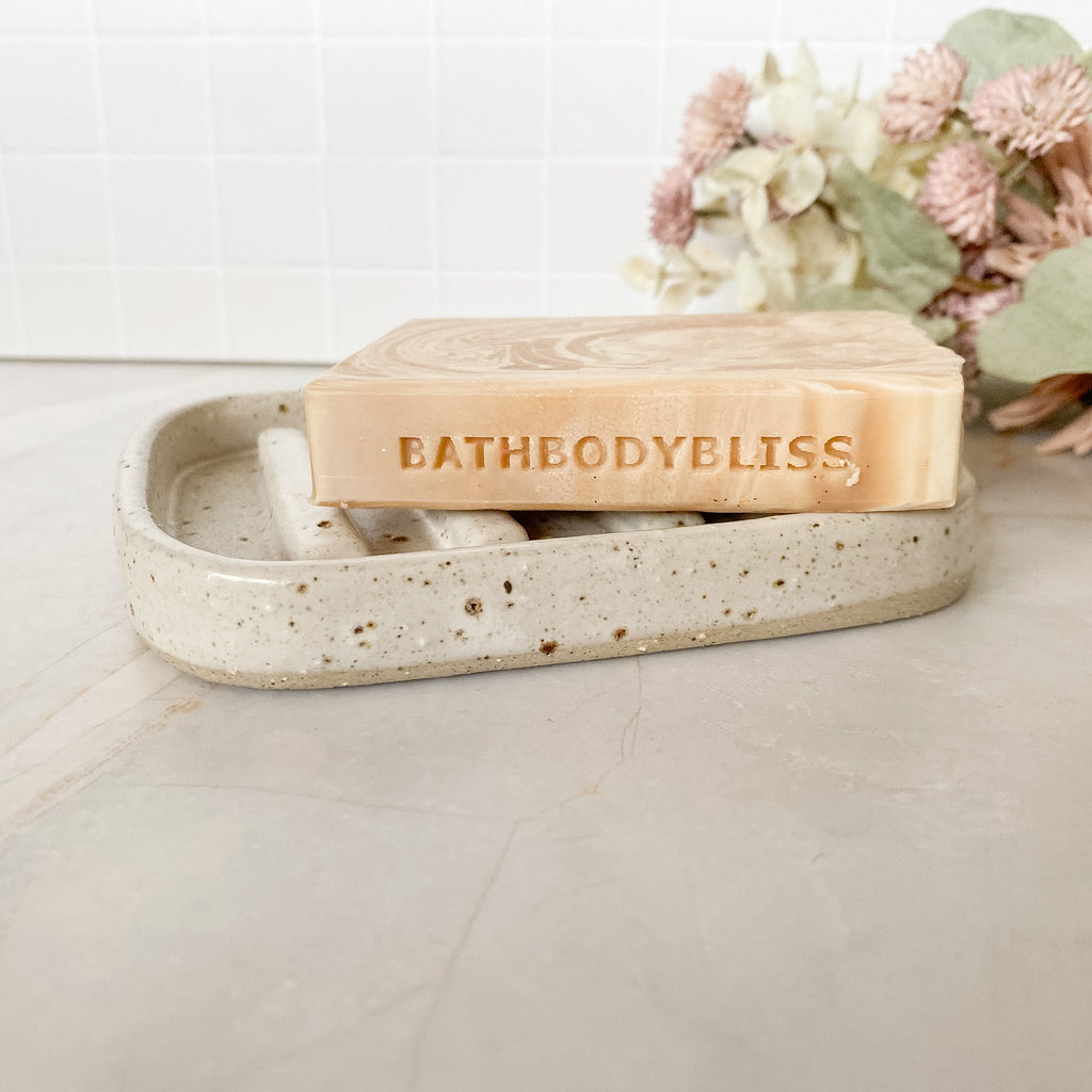 Bar of soap with 'BathBodyBliss' branding in a decorative dish on a neutral background.