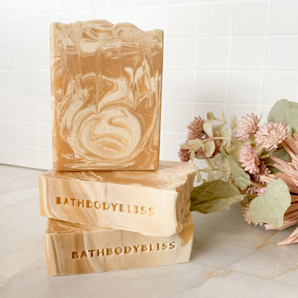 Three swirled soap bars with 'BathBodyBliss' branding on a marble surface with flowers.