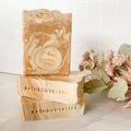Three swirled soap bars with 'BathBodyBliss' branding on a marble surface with flowers.