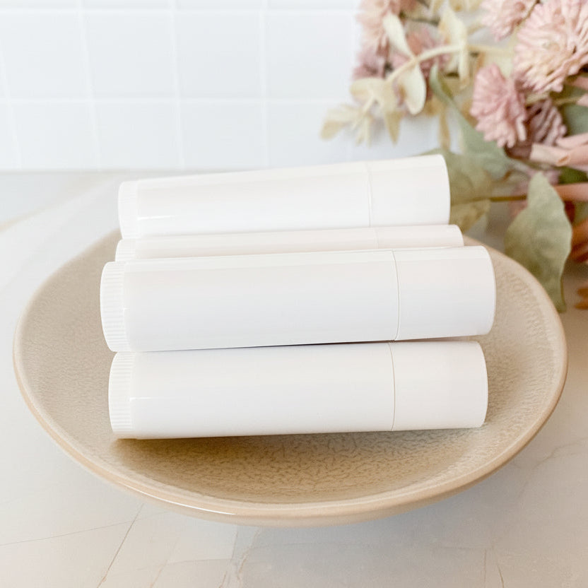 stack of  white lip balm tubes on a ceramic plate with a floral arrangement in the background.