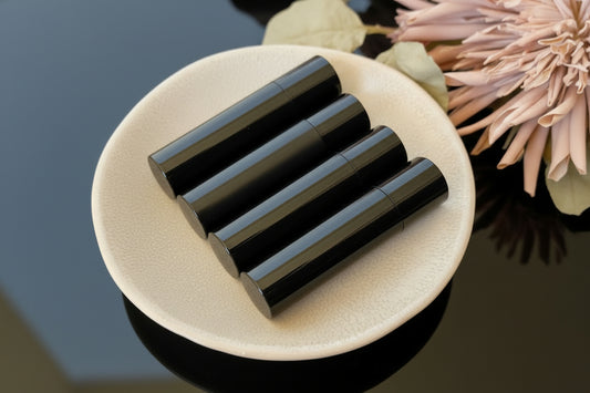 Four black tubes of handmade lip balm placed in a ceramic dish with a floral decoration in the background.